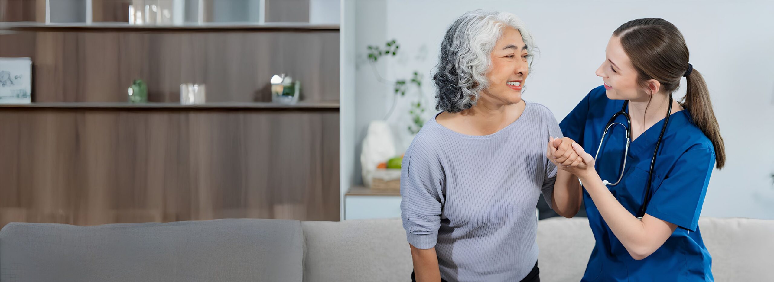 A caregiver in blue scrubs gently holds the hands of an elderly person, offering comfort and support.